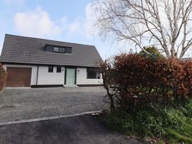 A detached house with a tiled roof and garage with gravel driveway and hedge in front at Badachro in Lesbury