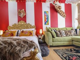 A bedroom with a gold ornate bed frame two animal head wall mounts a green sofa with patterned pillows and red and white striped walls at Circus Circus in Holywell