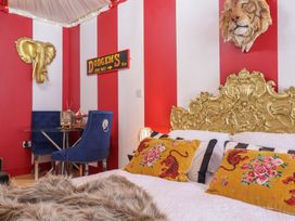 A bedroom with a gold ornate headboard pillows with tiger designs a faux fur blanket red and white striped walls a small glass table with blue chairs and a golden elephant wall decoration at Circus Circus in Holywell