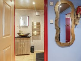 A bathroom with a wooden cabinet and bowl sink next to a gold towel rack and a wavy gold mirror on a blue wall at Circus Circus in Holywell