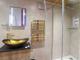 A bathroom with a glass shower enclosure a gold towel radiator a vessel sink with a gold faucet and a mirror at Circus Circus in Holywell
