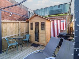 A small outdoor patio with wooden deck flooring a wooden shed a round table with two chairs a barbecue grill and two reclining lounge chairs at Circus Circus in Holywell