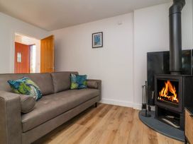 A living room with a brown sofa and two green leaf patterned cushions a wood burning stove with firewood and a small framed picture on the wall at Ladybird Rest in Parkham near Bideford
