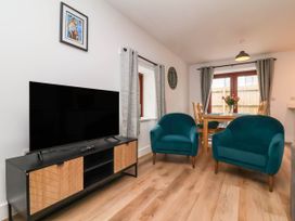 A living room with a television on a wooden cabinet two blue armchairs a wooden dining table with chairs and flowers at Ladybird Rest in Parkham near Bideford
