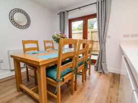 A dining room with a wooden table and six chairs with cushions and placemats with glass doors and curtains at Ladybird Rest in Parkham near Bideford