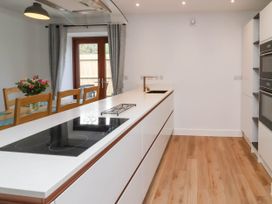 A kitchen with a white island countertop with a black stove and sink wooden chairs and a dining table with flowers near glass doors with curtains at Ladybird Rest in Parkham near Bideford