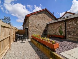 An outdoor patio with a stone building wooden fence black chairs and table and raised planters at Ladybird Rest in Parkham near Bideford