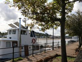 A boat docked by a riverside walkway with trees and benches at Ladybird Rest Parkham near Bideford