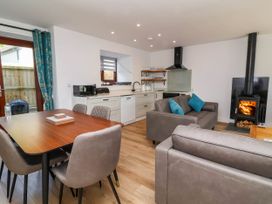 A kitchen and living area with a dining table and chairs a sofa with blue cushions and a wood burning stove at Bumblebee Meadows in Parkham near Bideford