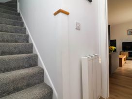 A carpeted staircase next to a white wall radiator and a glimpse of a living room with a television and wooden furniture at Bumblebee Meadows in Parkham near Bideford