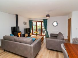 A living room with two grey sofas a coffee table with flowers a wood burning stove a television and sliding glass doors with curtains at Bumblebee Meadows in Parkham near Bideford