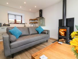 A living room with a gray sofa and blue pillows a wood burning stove and a wooden coffee table at Bumblebee Meadows in Parkham near Bideford