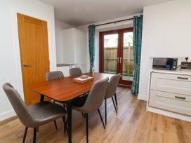A dining area with a wooden table and six chairs next to glass doors with blue curtains at Bumblebee Meadows in Parkham near Bideford
