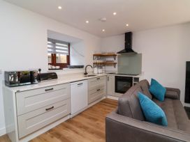 A kitchen area with white cabinets a dishwasher microwave oven and a gray sofa with blue cushions at Bumblebee Meadows in Parkham near Bideford