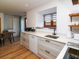 A kitchen with a sink dishwasher microwave toaster and kettle next to a dining table with chairs at Bumblebee Meadows in Parkham near Bideford