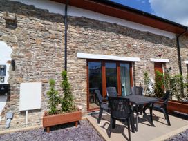 Outdoor patio area with black plastic table and chairs in front of stone wall building at Bumblebee Meadows Parkham near Bideford