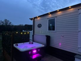 A hot tub with purple lights next to a caravan with exterior string lights at Swan Lodge in Swannington near Coalville