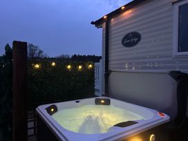 An outdoor hot tub with water illuminated at dusk next to a caravan with lights and greenery at Swan Lodge in Swannington near Coalville
