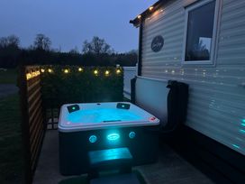 An outdoor hot tub with blue lights next to a mobile home with string lights at Swan Lodge in Swannington near Coalville