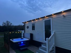 An outdoor hot tub next to a mobile home with steps and string lights at Swan Lodge in Swannington near Coalville