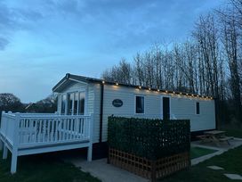 A mobile home with a white deck and string lights next to leafless trees at Swan Lodge in Swannington near Coalville