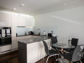 A modern kitchen with white cabinets grey countertops a glass dining table with black chairs and kitchen appliances at Apartment 17 Abbey Sands in Torquay