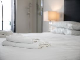 Folded white towels on a bed with pillows and a lamp in the background at Apartment 17 Abbey Sands in Torquay