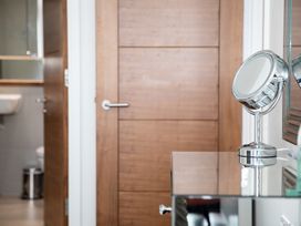 A round makeup mirror on a reflective surface with a wooden door and a bathroom in the background at Apartment 17 Abbey Sands Torquay