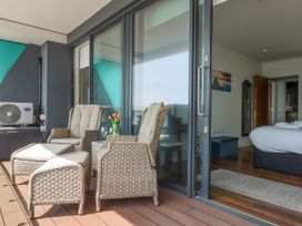 A balcony with wicker chairs and ottomans next to a sliding glass door leading to a bedroom at Apartment 17 Abbey Sands in Torquay