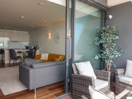 A living area with gray and orange sofas next to a dining table and kitchen with white cabinets and an outdoor seating area with wicker chairs and a potted plant at Apartment 17 Abbey Sands in Torquay