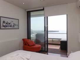 A bedroom with a bed a red chair with cushions a framed painting and a glass door leading to a balcony at Apartment 17 Abbey Sands in Torquay
