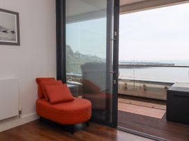 A red chaise lounge chair next to a glass sliding door leading to a balcony with a view of the sea at Apartment 17 Abbey Sands in Torquay