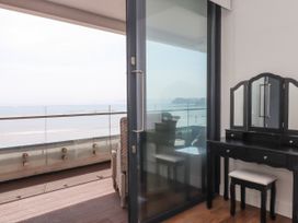 A dressing table with a stool next to a glass sliding door leading to a balcony with wicker chairs and a view of the sea at Apartment 17 Abbey Sands in Torquay