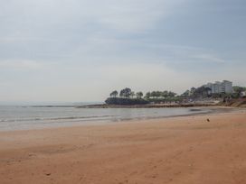 A sandy beach with calm sea and a tree-covered cliff with buildings in the background at Apartment 17 Abbey Sands in Torquay