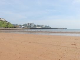 A sandy beach with people near the water and buildings on cliffs in the background at Apartment 17 Abbey Sands in Torquay