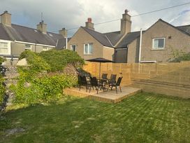 A backyard with a wooden deck and outdoor table with six chairs and an umbrella at 1 Mona Terrace in Llanfachraeth