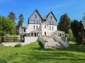 A large house with two conservatories and stairs leading down to a grassy yard surrounded by trees at Serenity House The Retreat in Llangammarch Wells near Llanwrtyd Wells