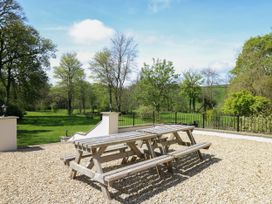 An outdoor seating area with two wooden picnic tables on a gravel surface overlooking a lawn with trees at Serenity House The Retreat in Llangammarch Wells near Llanwrtyd Wells