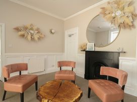 A sitting area with three chairs around a wooden coffee table near a black fireplace with a round mirror and dried flower arrangements at Serenity House The Retreat in Llangammarch Wells near Llanwrtyd Wells