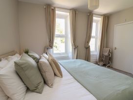 A bedroom with a bed with pillows and a blanket two windows with curtains and a door at Serenity House The Retreat in Llangammarch Wells near Llanwrtyd Wells