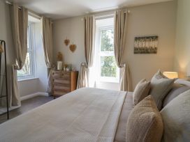 A bedroom with a bed, pillows, a lamp, a wooden chest of drawers, curtains, and wall decorations at Serenity House The Retreat in Llangammarch Wells near Llanwrtyd Wells