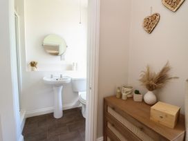 A bathroom with a pedestal sink toilet round mirror and a wooden dresser with decorative items at Serenity House The Retreat in Llangammarch Wells near Llanwrtyd Wells