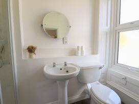 A bathroom with a pedestal sink a toilet rolls a round mirror and a window at Serenity House The Retreat in Llangammarch Wells near Llanwrtyd Wells