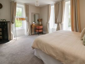A bedroom with a bed a study desk and chair a clothing rack and large windows with curtains at Serenity House The Retreat Llangammarch Wells near Llanwrtyd Wells