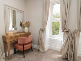 A bedroom corner with a wooden dressing table, a mirror, a pink chair, beige curtains, and a window at Serenity House The Retreat in Llangammarch Wells near Llanwrtyd Wells