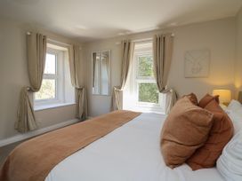 A bedroom with two windows beige curtains bed with brown pillows and a lamp on a side table at Serenity House The Retreat Llangammarch Wells near Llanwrtyd Wells