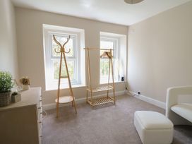 A room with a chest of drawers plants wooden coat rack wooden clothing rack with hangers white armchair and ottoman at Serenity House The Retreat in Llangammarch Wells near Llanwrtyd Wells