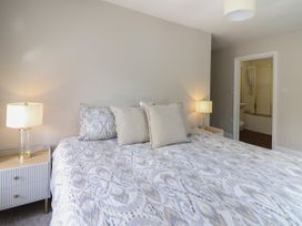 A bedroom with a patterned bedspread, pillows, two bedside tables with lamps and an open door to a bathroom at Serenity House, The Retreat in Llangammarch Wells near Llanwrtyd Wells