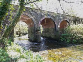 A stone bridge with three arches over a flowing river with trees and bushes nearby at Serenity House The Retreat in Llangammarch Wells near Llanwrtyd Wells