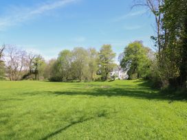 A large green field with trees and a white house in the background at Serenity House The Retreat in Llangammarch Wells near Llanwrtyd Wells